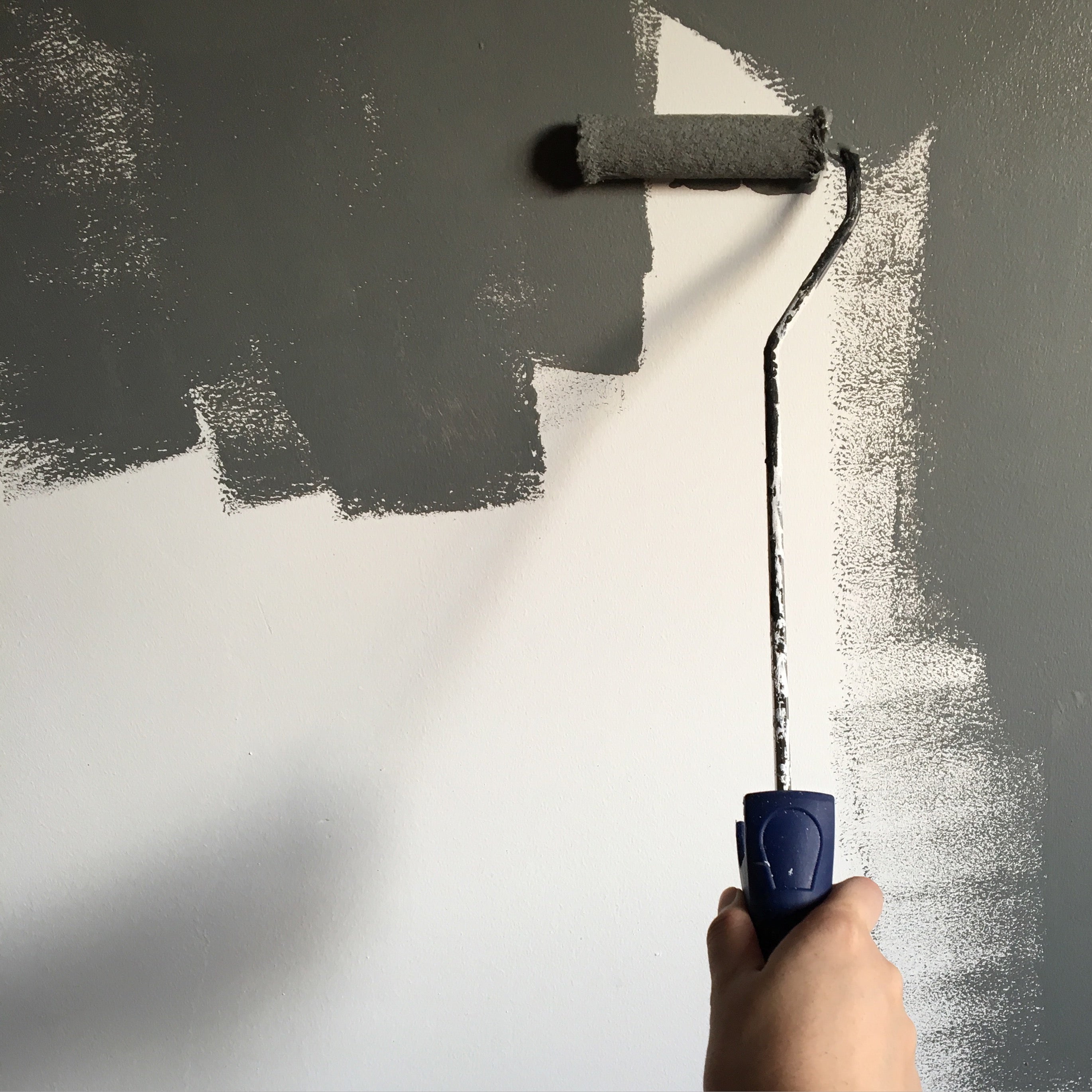 person-holding-paint-roller-while-painting-the-wall